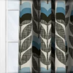 Stylish teal and grey leaf-patterned curtain in sunlit room.