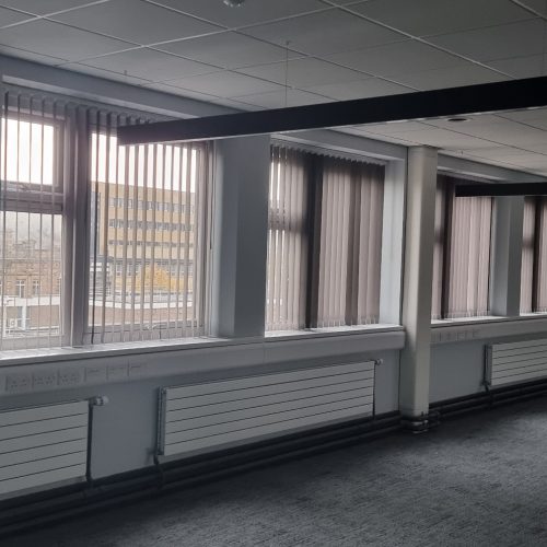 Dimly lit office with vertical blinds and building view.