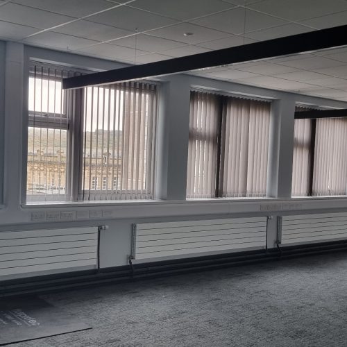 Empty room with large, curtained windows and grey carpet.