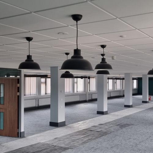 Modern office interior with hanging lamps and columned walkway.